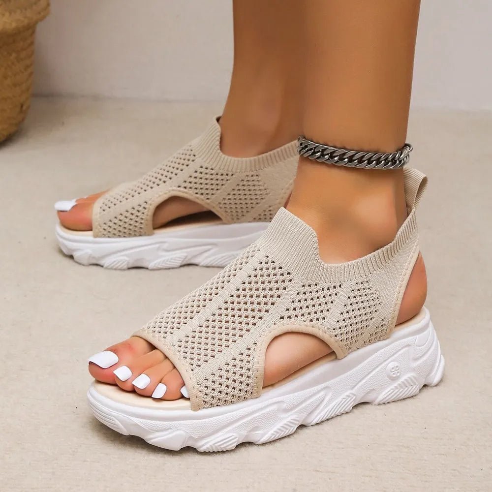 Beige open-knit slip-on sandals with side cutouts and chunky white soles, shown on feet