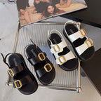 Black and white double-strap platform sandals with gold-tone buckles and slingback straps on a glass tray