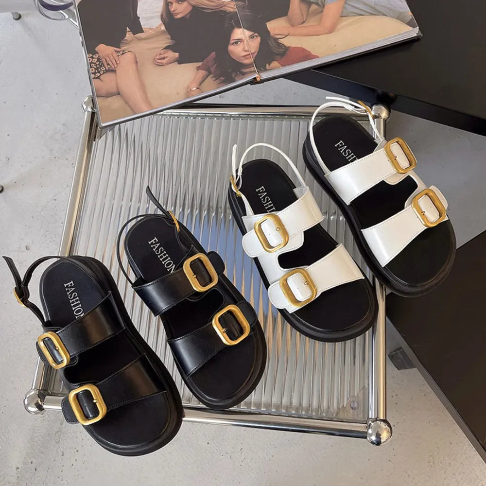 Black and white double-strap platform sandals with gold-tone buckles and slingback straps on a glass tray