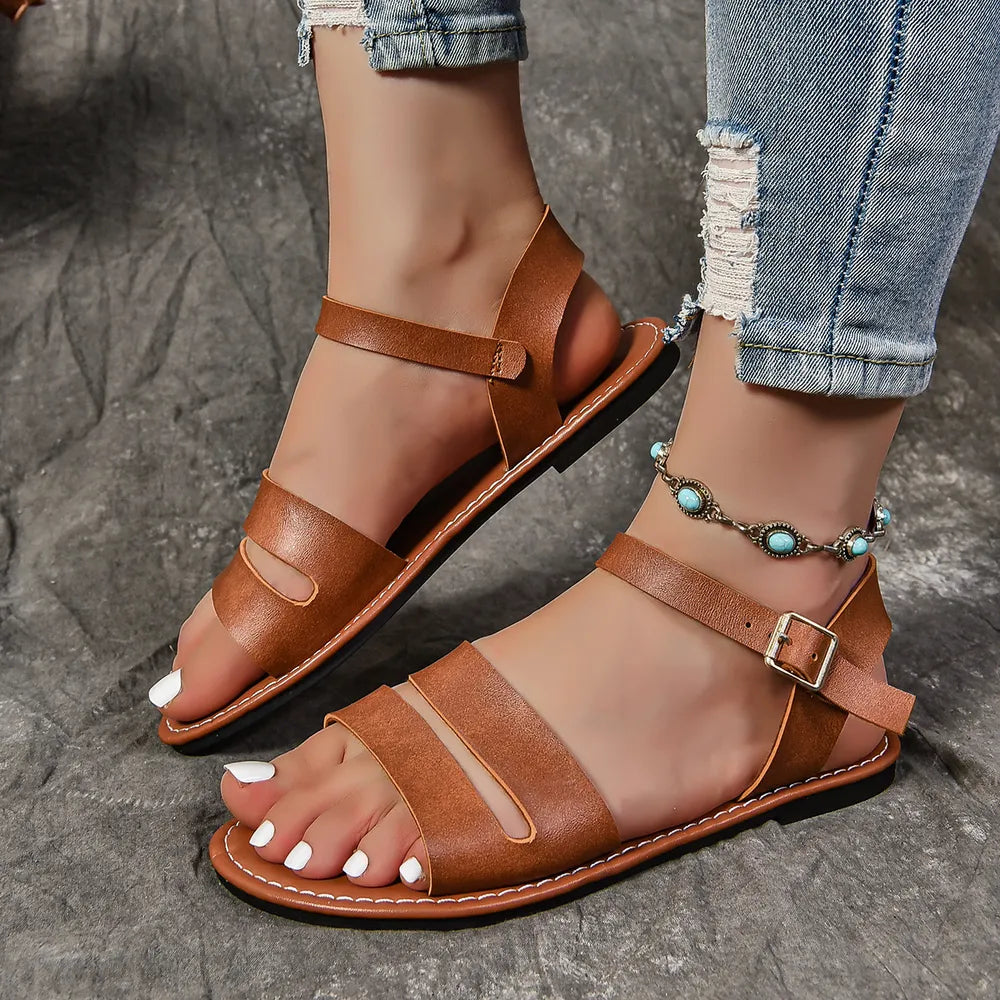 Tan faux leather flat sandals with two wide toe bands and a buckled ankle strap, shown on feet