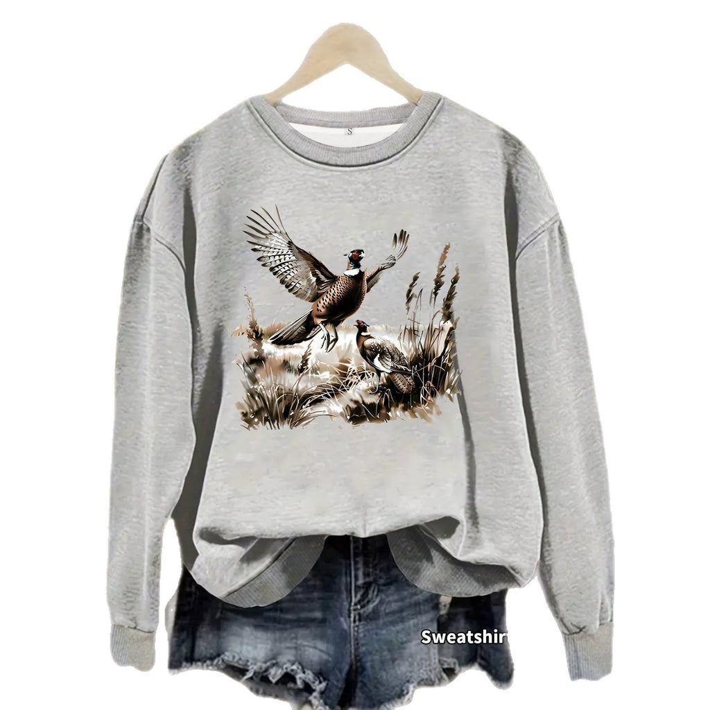 Gray Pheasant Print Crewneck Fleece Sweatshirt on a hanger over denim shorts