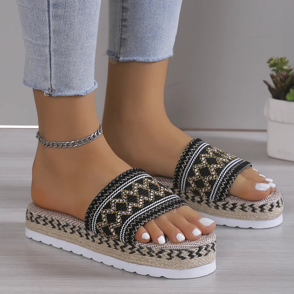 Black embroidered band platform slides with a geometric pattern and jute-look espadrille sole, shown on feet