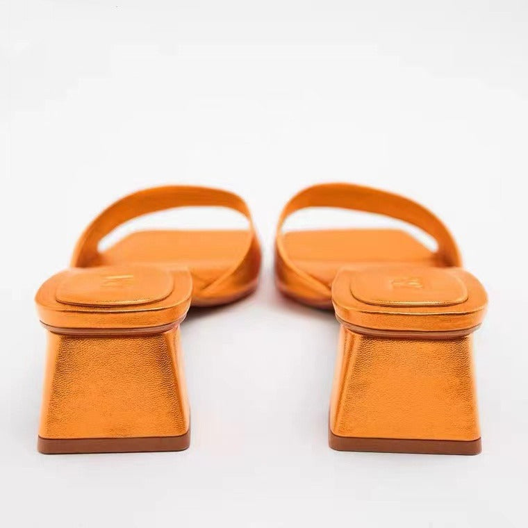 Pair of metallic orange square-toe mules with a wide strap and a low flared block heel on a white background